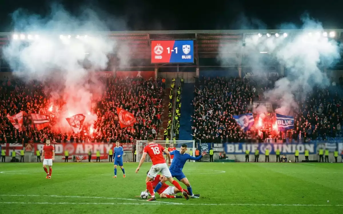 Jugadores de f&uacute;tbol en un derbi local con ambiente intenso en las gradas